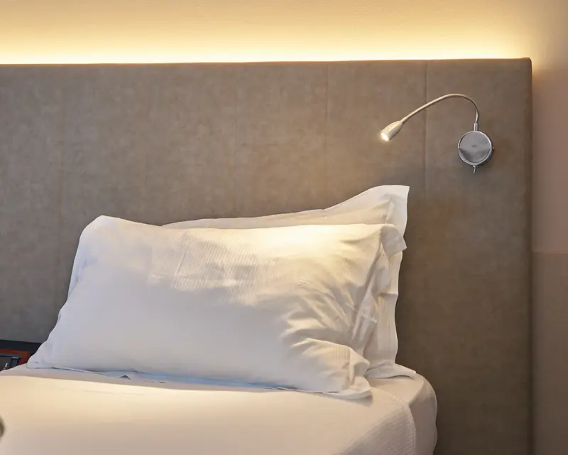 Da vicino: il cuscino bianco, la testata imbottita e la lampada da lettura accesa