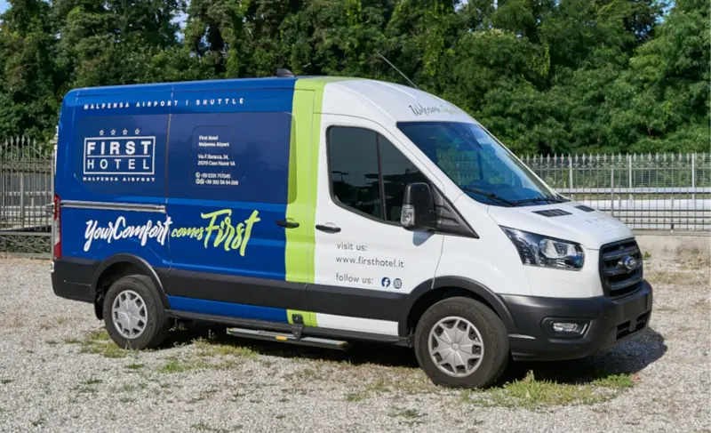 La navetta del First Hotel, blu e verde con la scritta YourComfort comes First, ferma sulla ghiaia